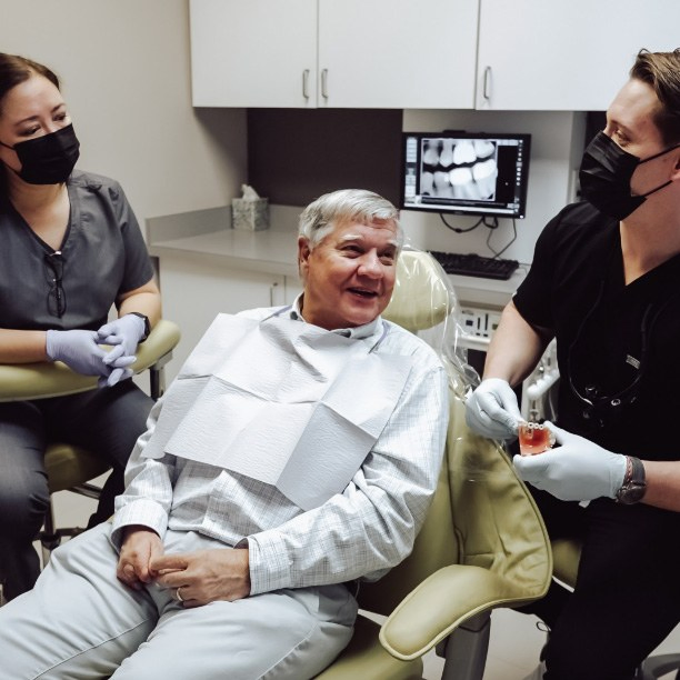 Dentist and dental team member talking to older man in dental chair