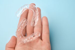 Hand holding 2 clear aligners over a pale blue background